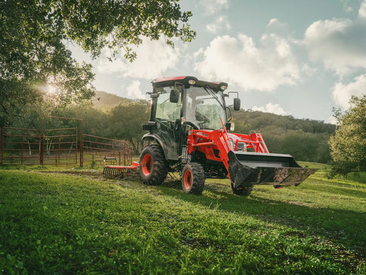 Kioti tractor with front loader in a grassy field with trees and mountains in the background