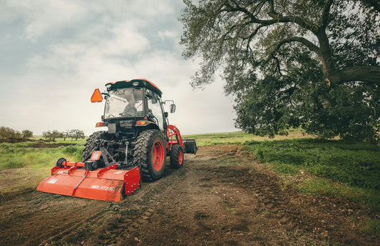 Red Kioti tractor on a dirt path with trees and open sky in the background