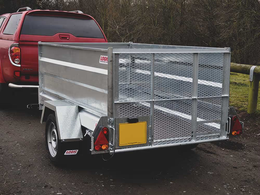 Metal trailer attached to a red pickup truck on a dirt road with trees in the background.