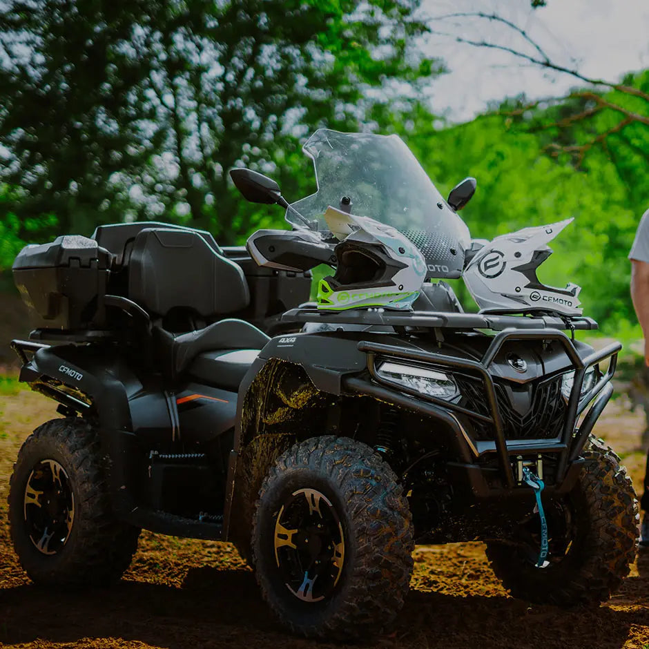 Black CFMOTO ATV with a helmet on top, surrounded by greenery