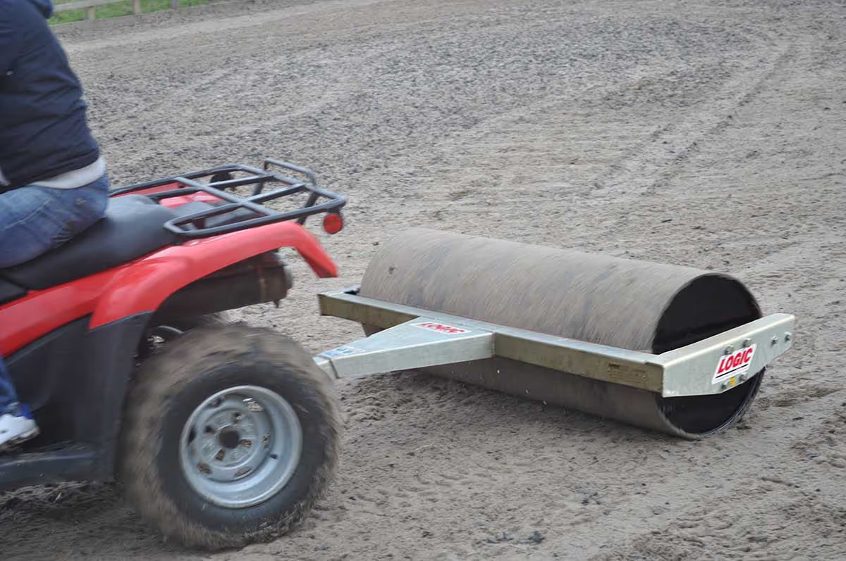Person operating a red ATV with a land roller attached on a dirt surface