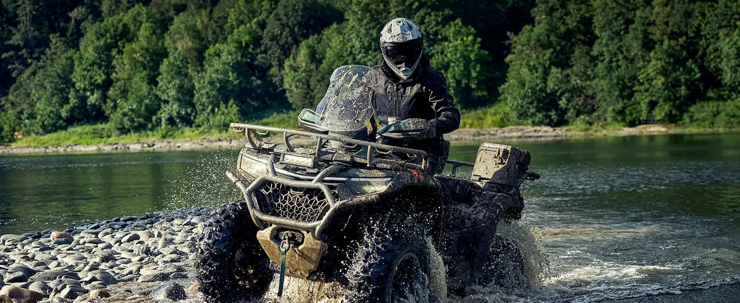 Person riding a CFMOTO ATV through a river with a forested area in the background