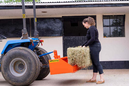 Person loading hay into a Fleming tractor transport box