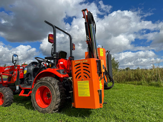 FarmMaster tractor hedge cutter attachment in a grassy field under a cloudy sky.