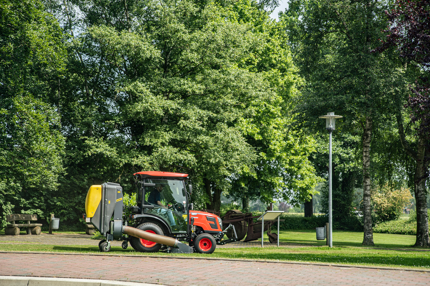 Small Kioti tractor with collector attachment on a road lined with trees