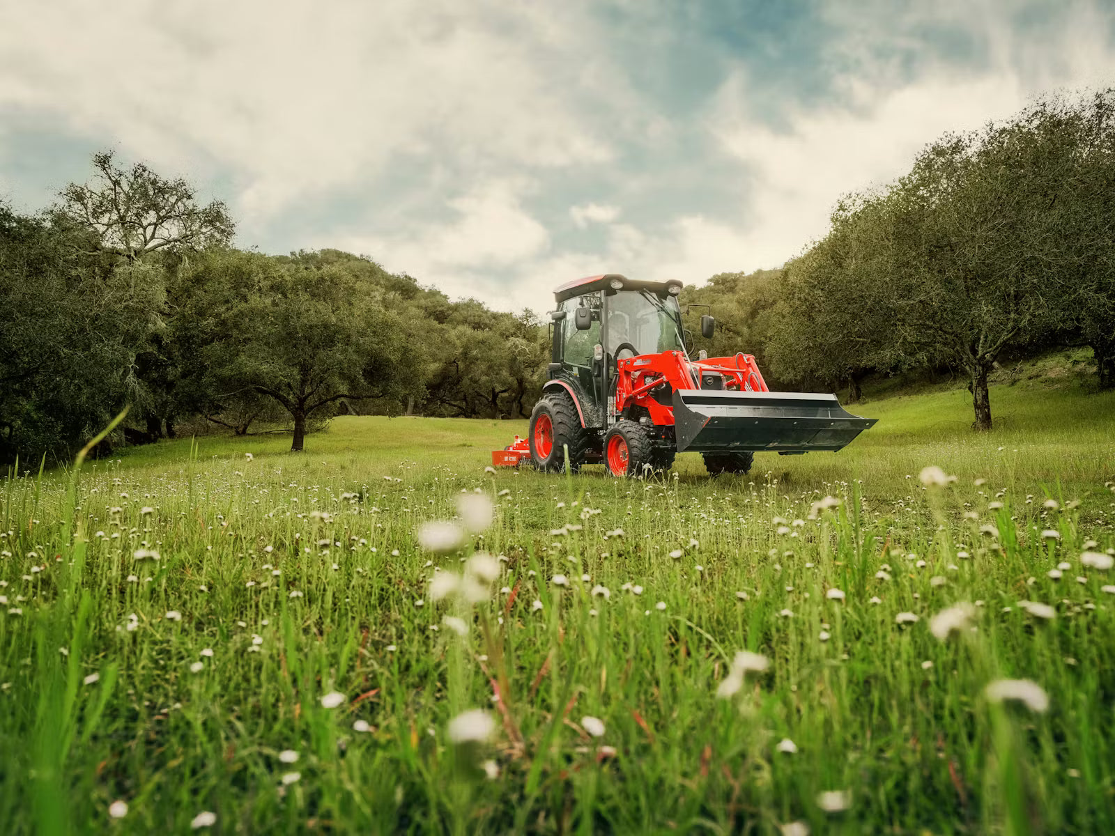 Kioti tractor in a field with trees and a cloudy sky