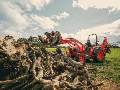 Red Kioti tractor with a front loader attached to a pile of logs under a cloudy sky.