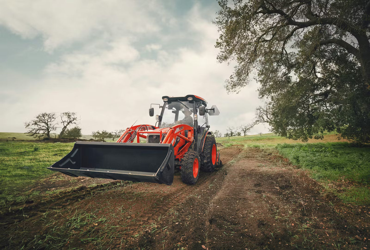 Orange Kioti tractor on a dirt path with trees and grass in the background