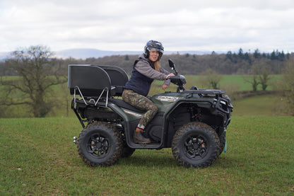Person riding a CFMOTO quad bike in a grassy field with trees in the background