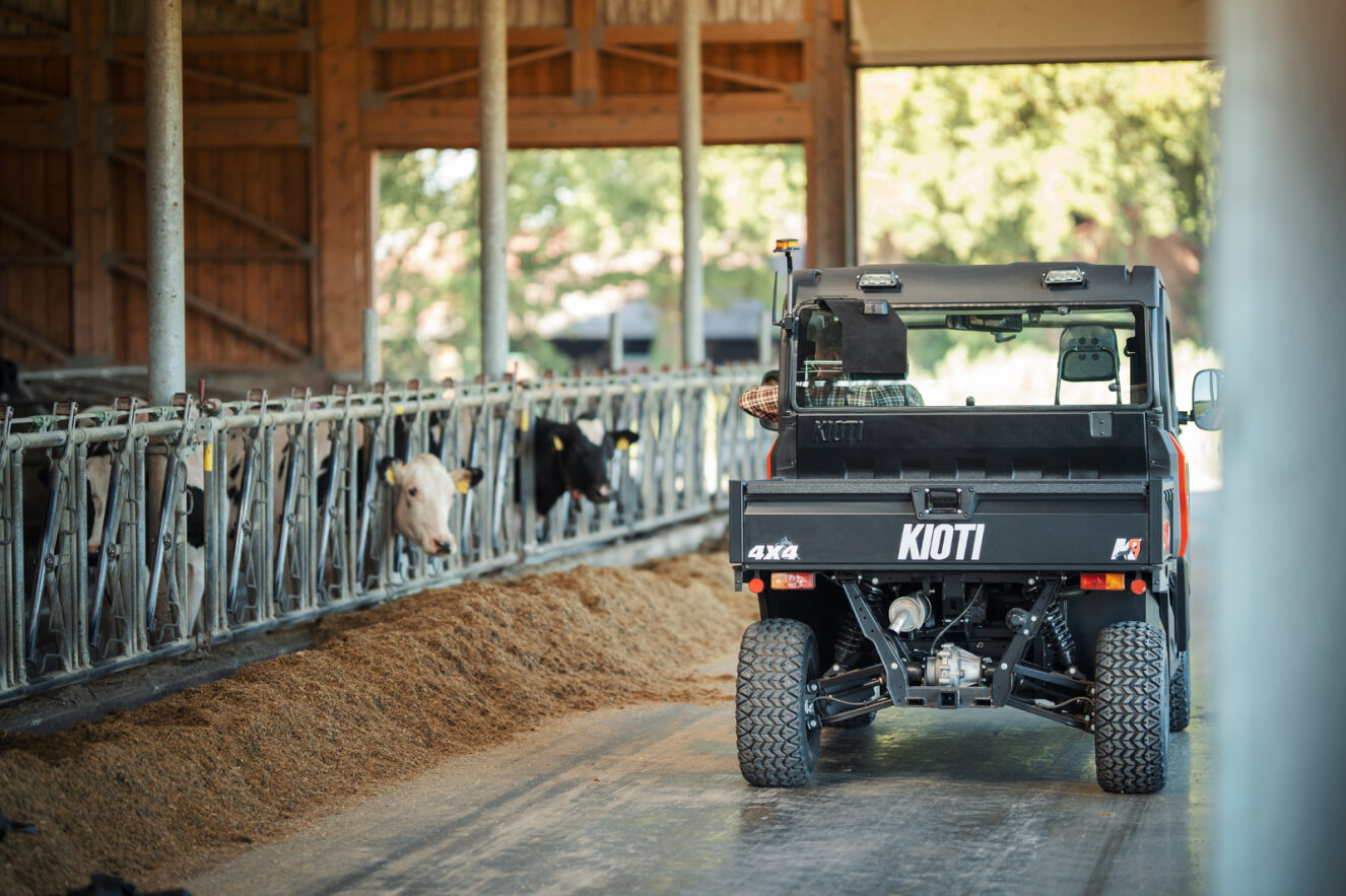 Truck labeled 'Kioti' in a barn with cows and hay.