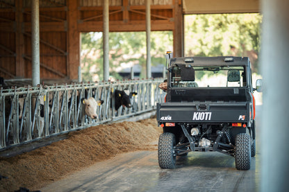 Truck labeled 'Kioti' in a barn with cows and hay.