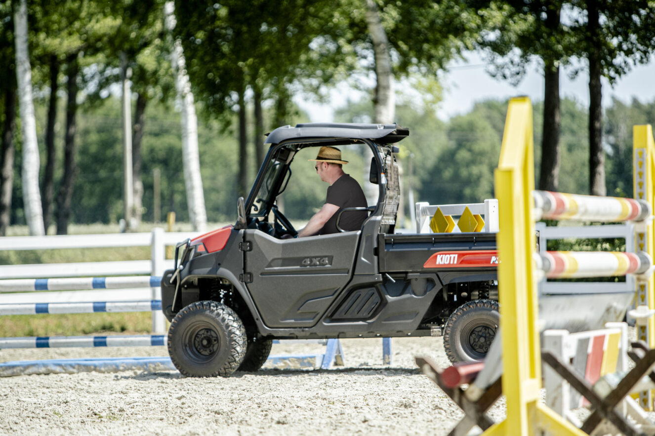 Person driving a Kioti K9 utility vehicle on a dirt path with trees in the background