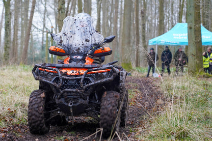 CFMOTO ATV in a forest setting, with people and a tent in the background.