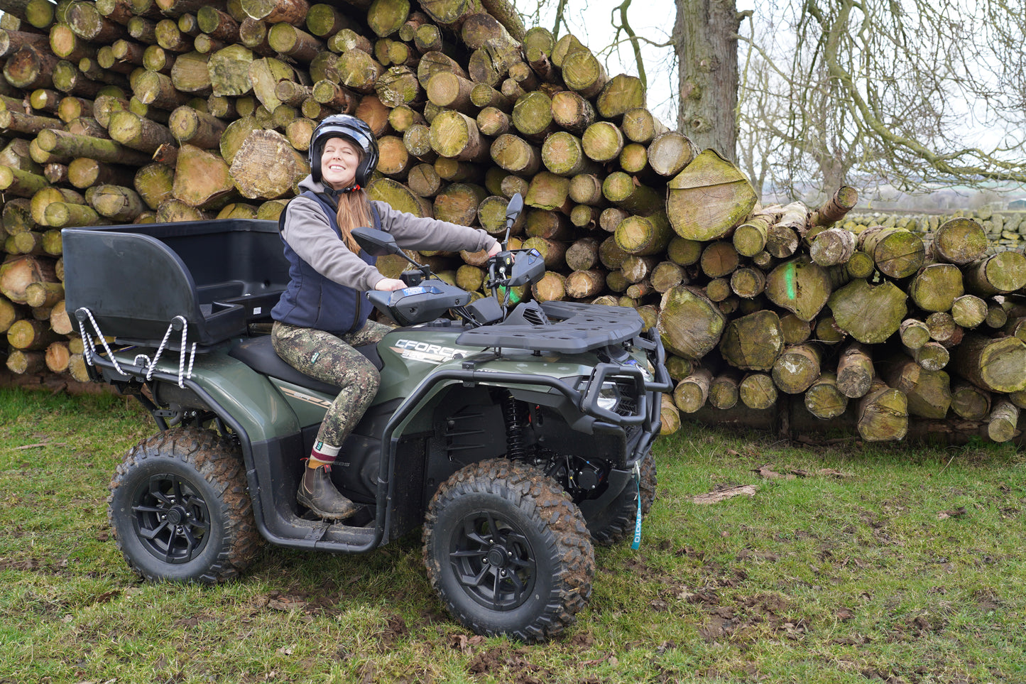 Person sitting on a CFMOTO four-wheeler in front of stacked logs