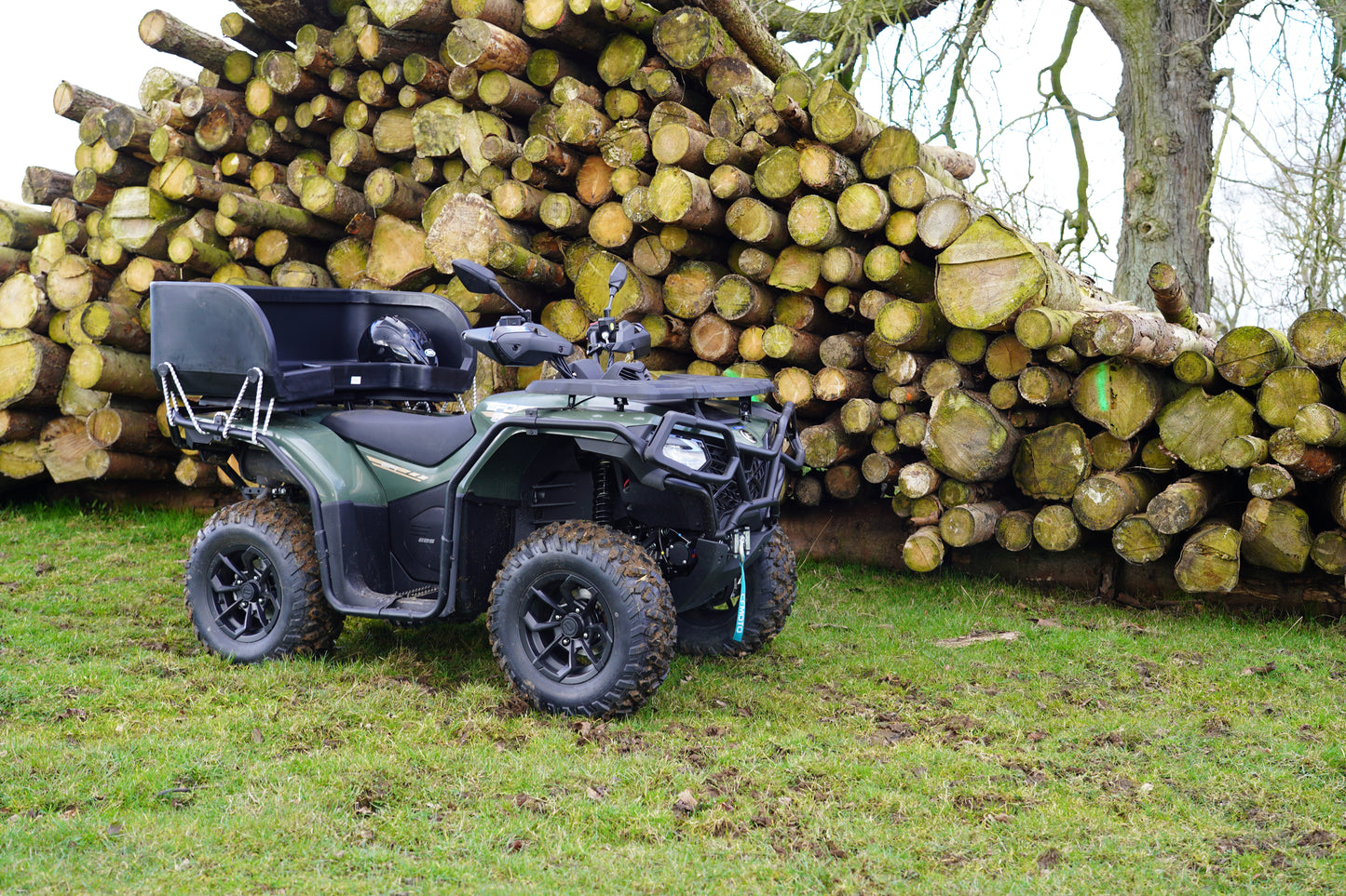 CFMOTO ATV parked in front of a stack of logs on a grassy area