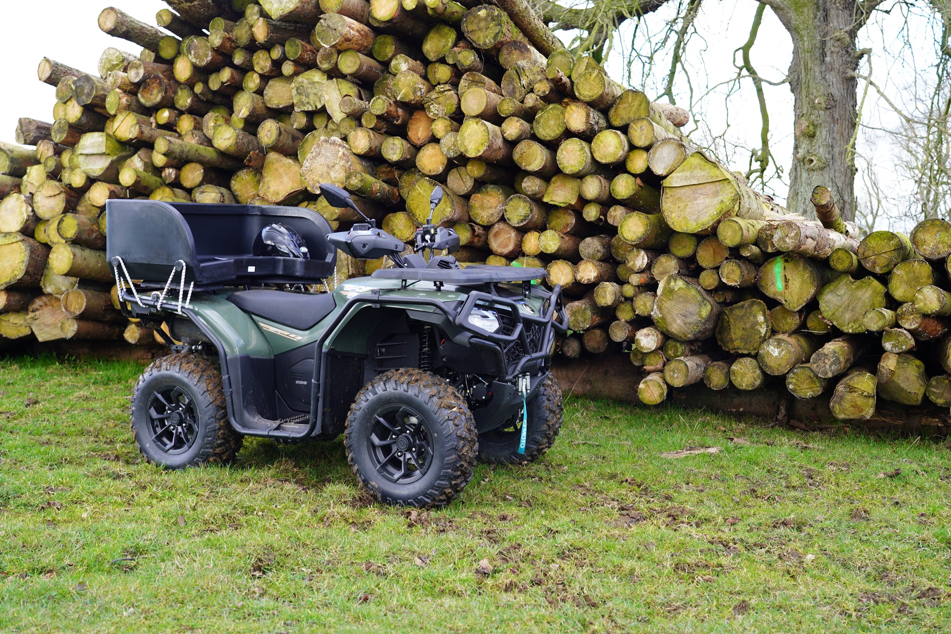 CFMOTO ATV parked in front of a stack of logs on a grassy area