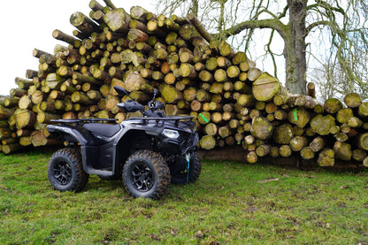 Black CFMOTO ATV parked in front of a large pile of logs in a forest setting