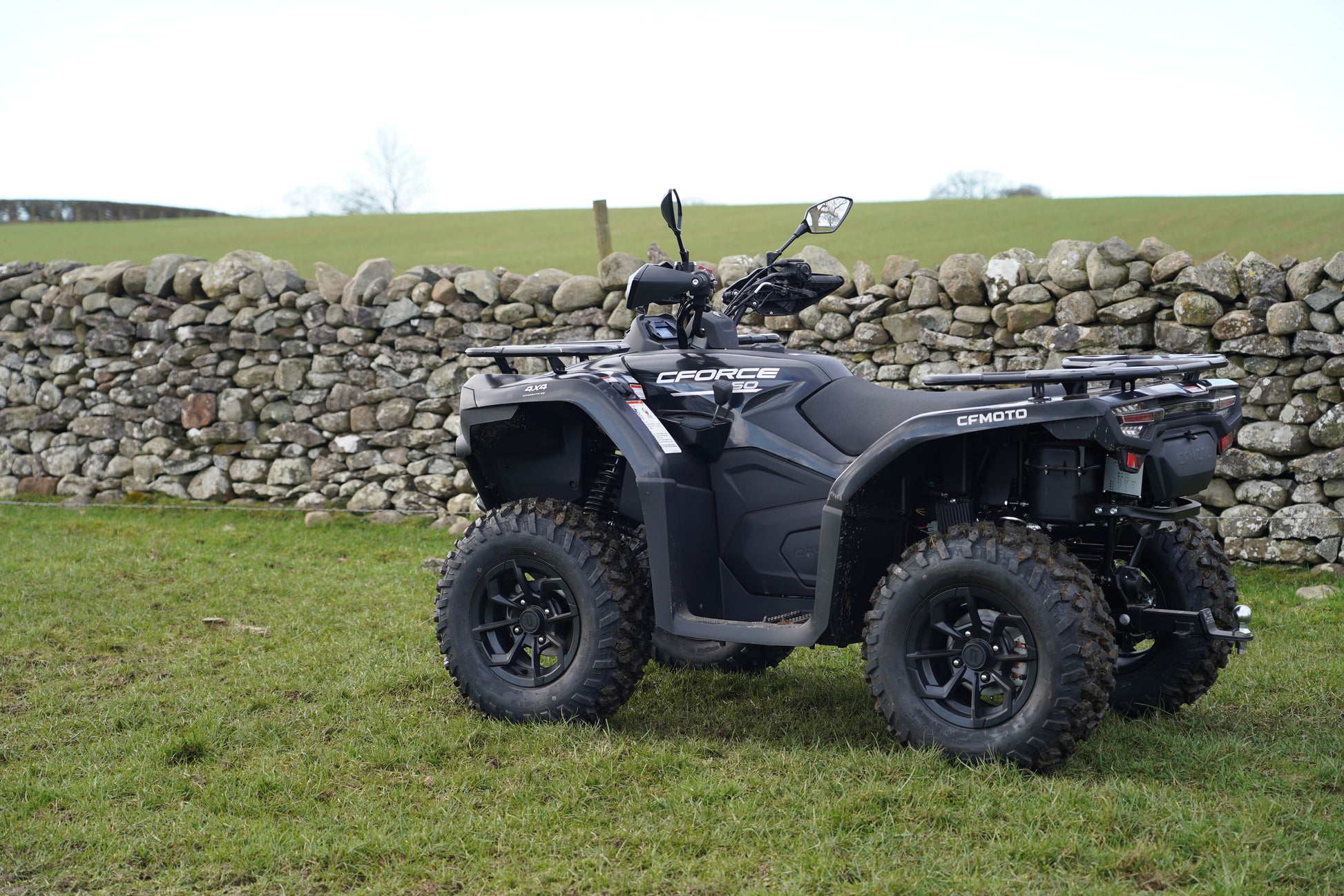 Black CFMOTO quad bike parked on grass with a stone wall in the background
