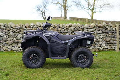 Black CFMOTO quad bike parked in a grassy field with a stone wall and trees in the background