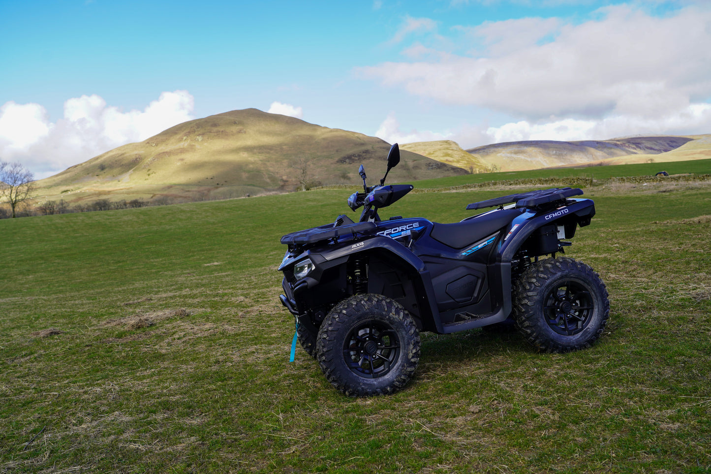 Black CFMOTO ATV parked on a grassy field with hills in the background