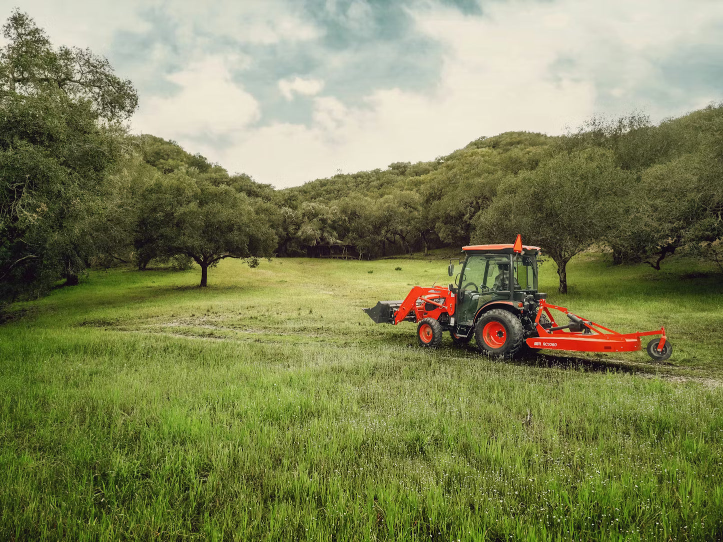 Kioti tractor in a grassy field with trees in the background