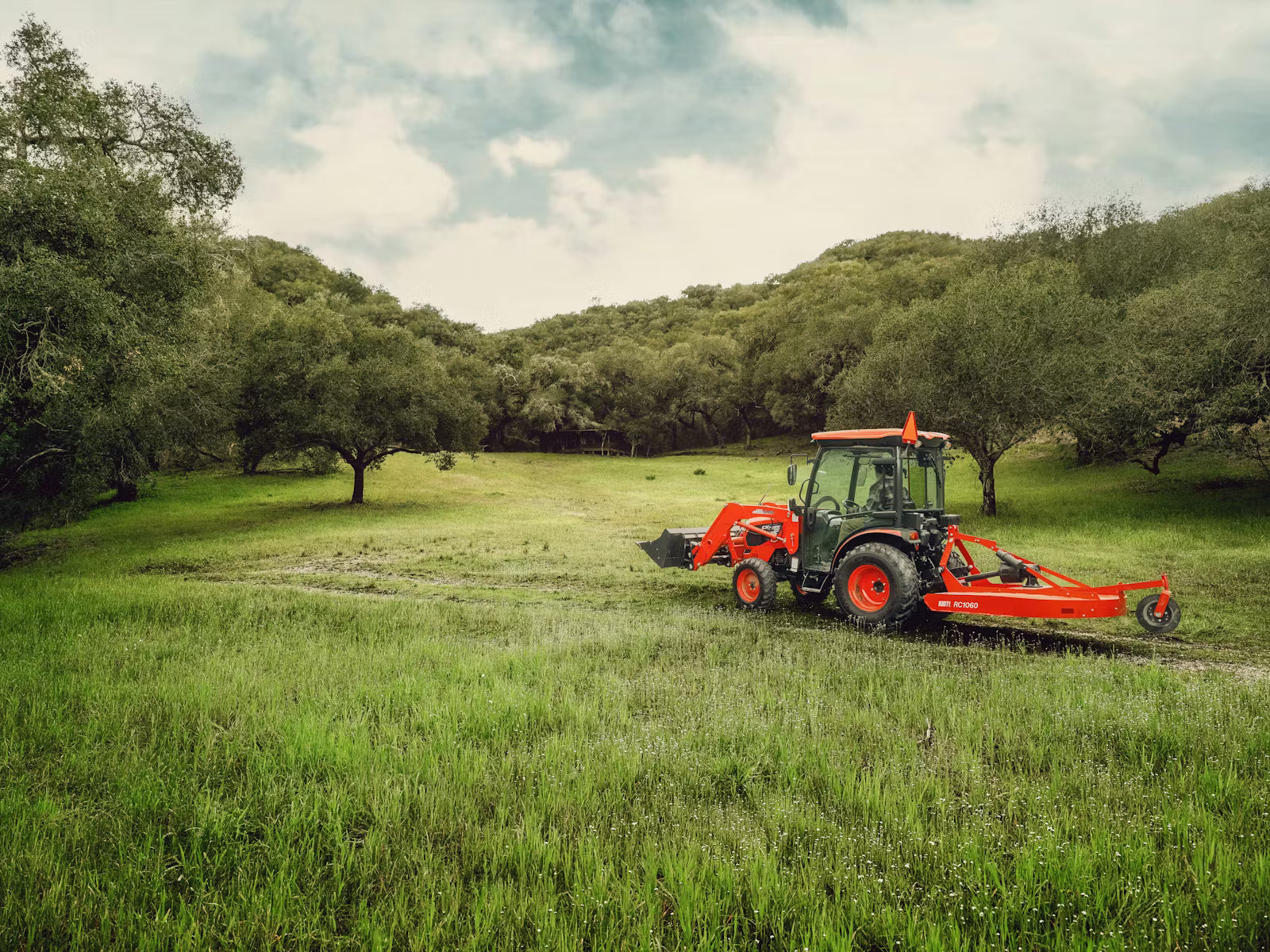 Kioti tractor in a grassy field with trees in the background