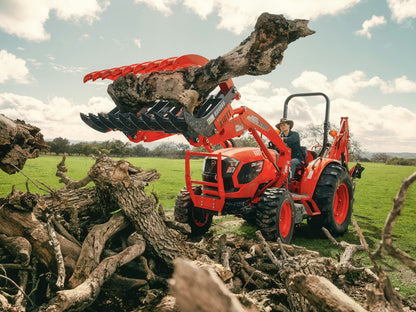 Red Kioti tractor lifting a large log in a field with a person operating it.