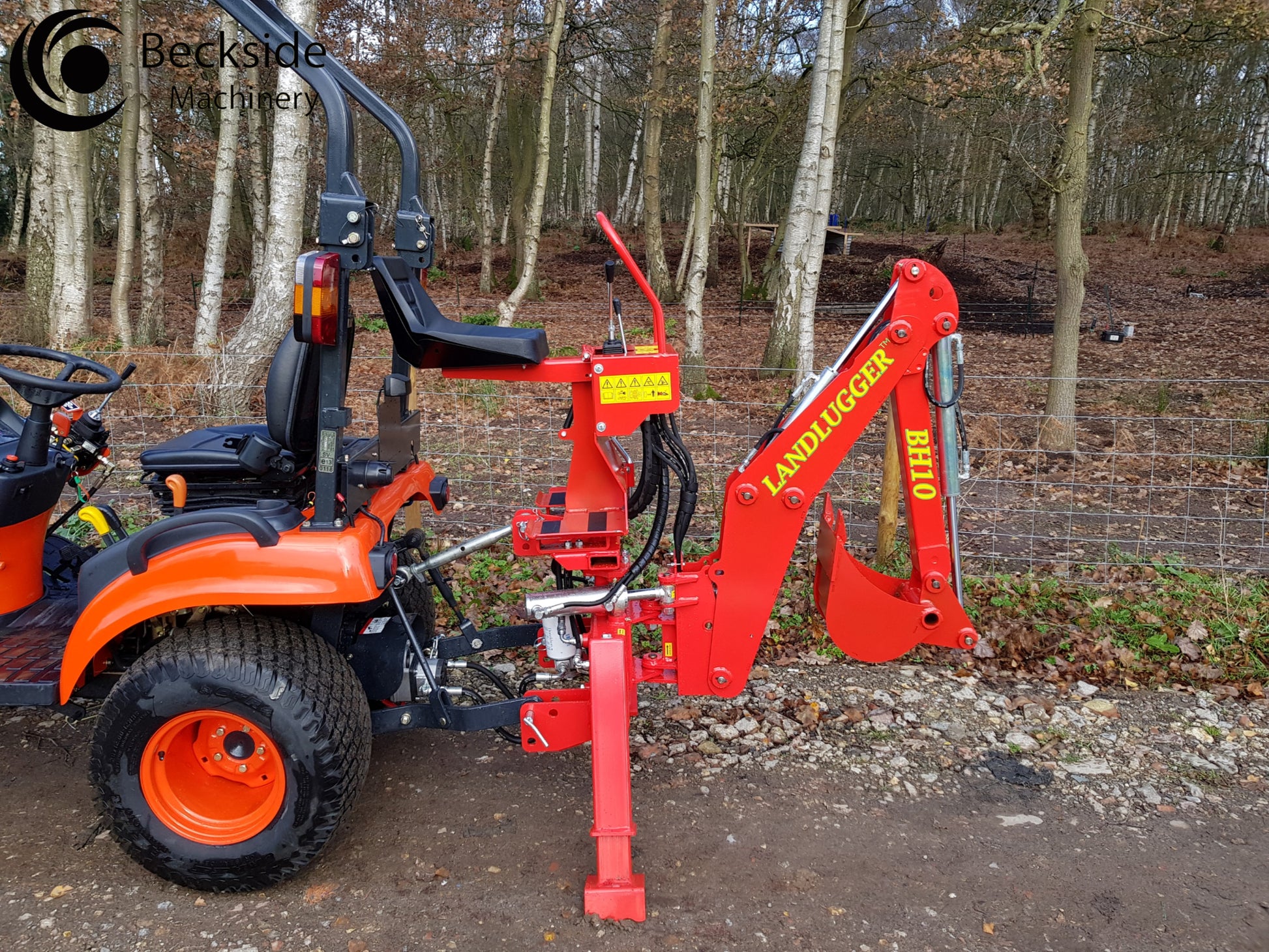 Orange tractor with a red FarmMaster tractor backhoe in a forest setting