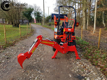 FarmMaster tractor backhoe on a gravel path in a wooded area.