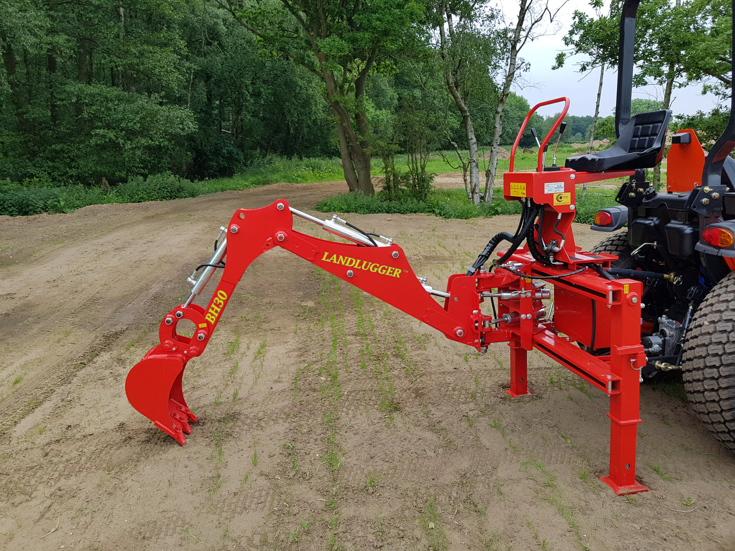 FarmMaster LandLugger tractor backhoe on a dirt road with trees in the background