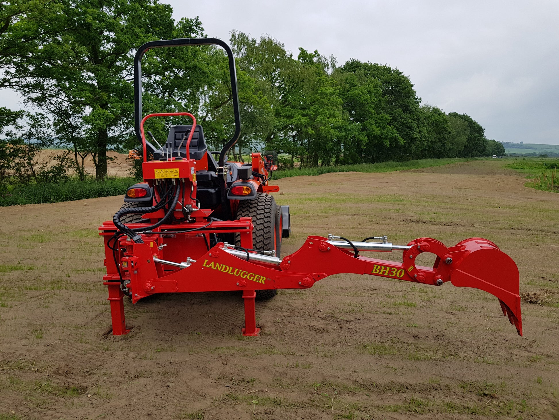 FarmMaster LandLugger tractor backhoe on a field with trees in the background