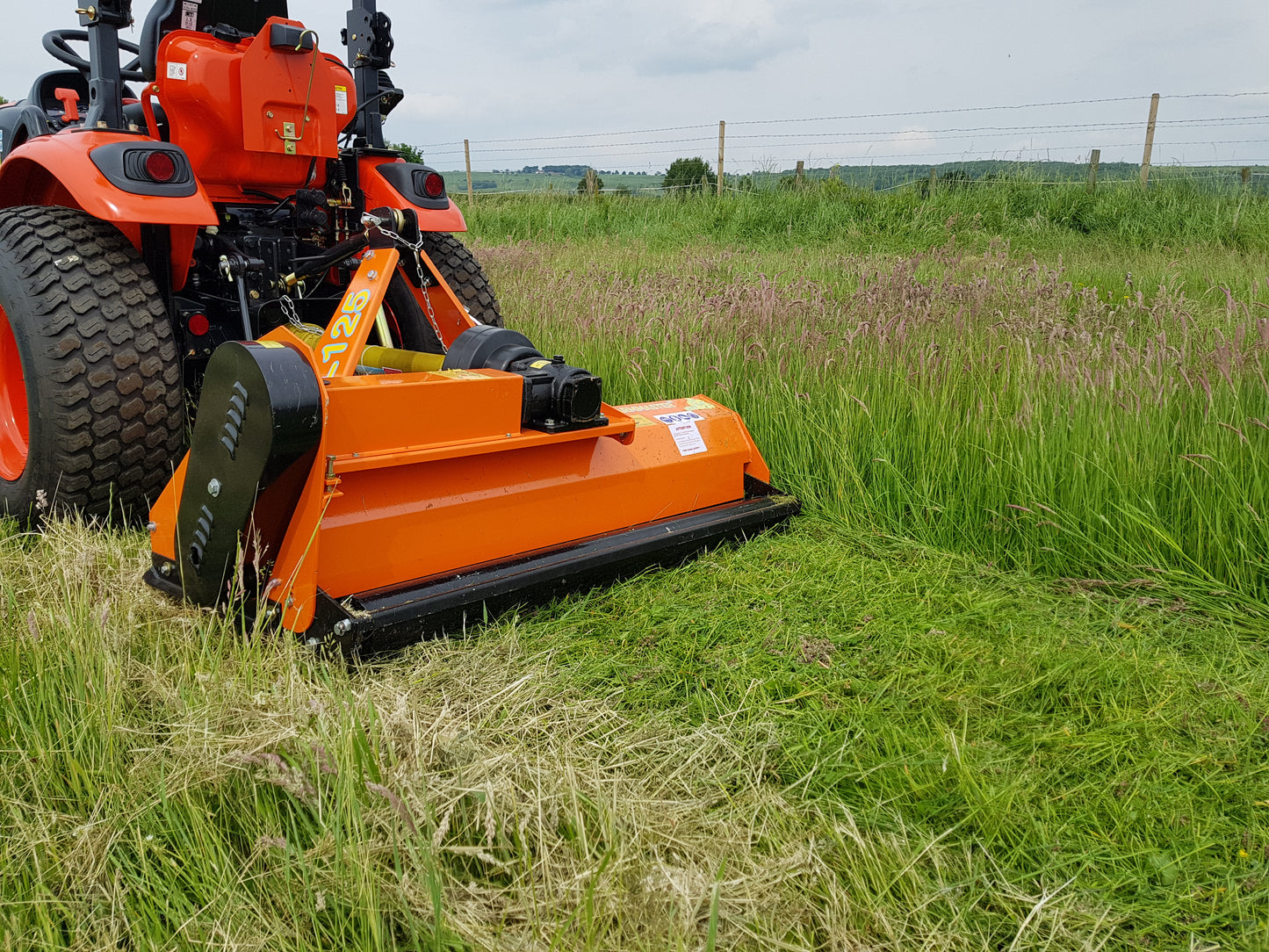 Kioti tractor with a flail mower attachment cutting through tall grass in an open field.