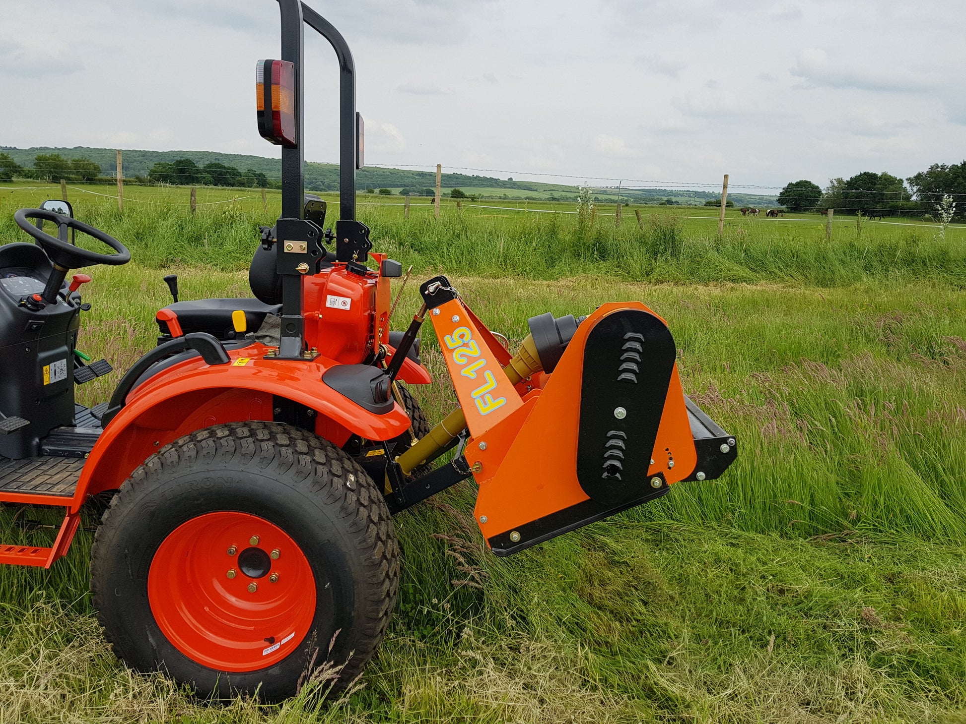 Orange tractor with a FarmMaster flail mower in a grassy field