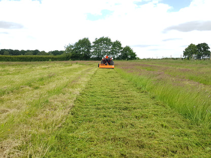 Tractor mowing a field with trees and blue sky in the background