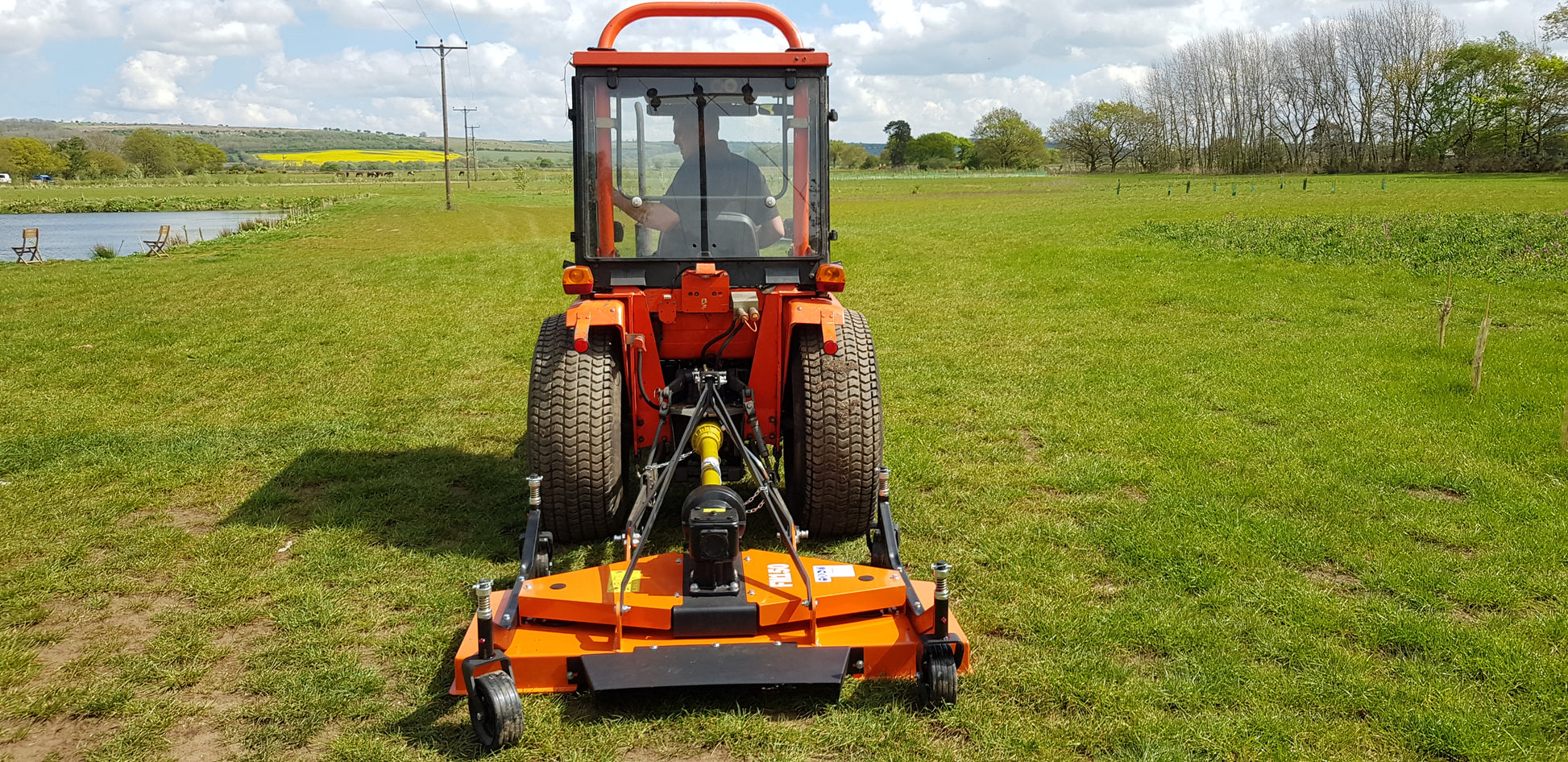 Orange tractor mowing a field with a scenic background
