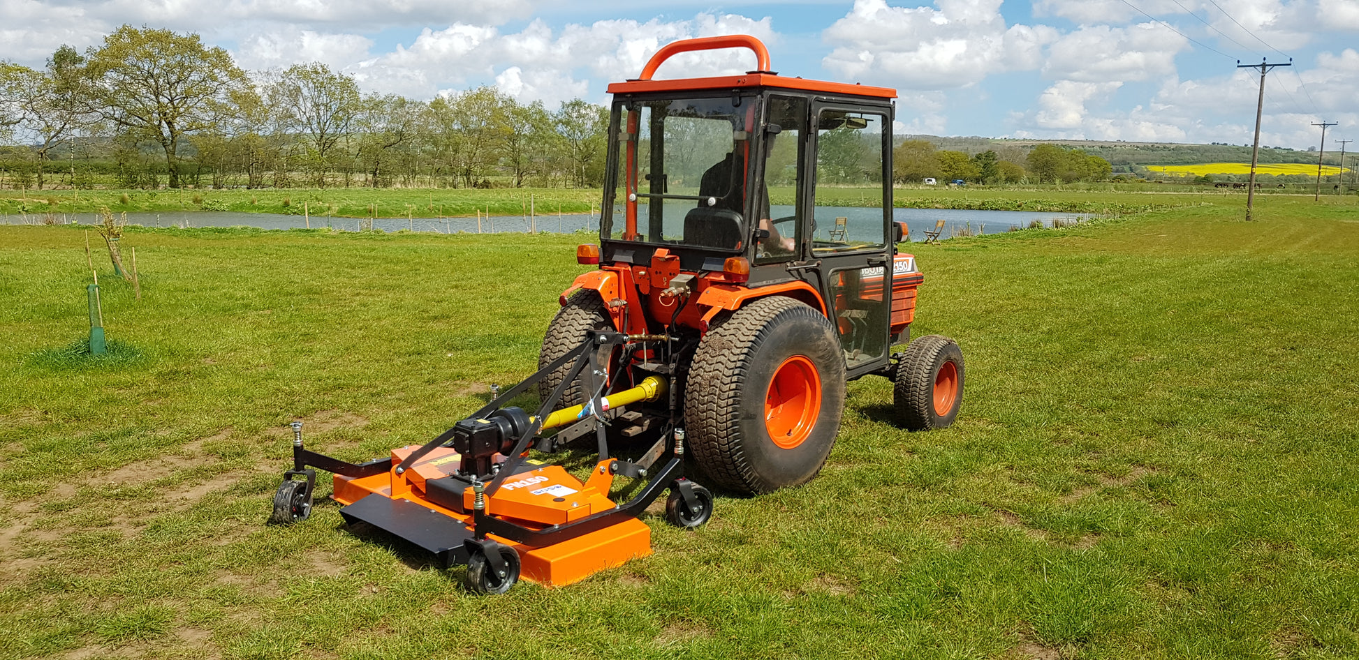 Orange tractor with a FarmMaster finishing mower attachment on a grassy field