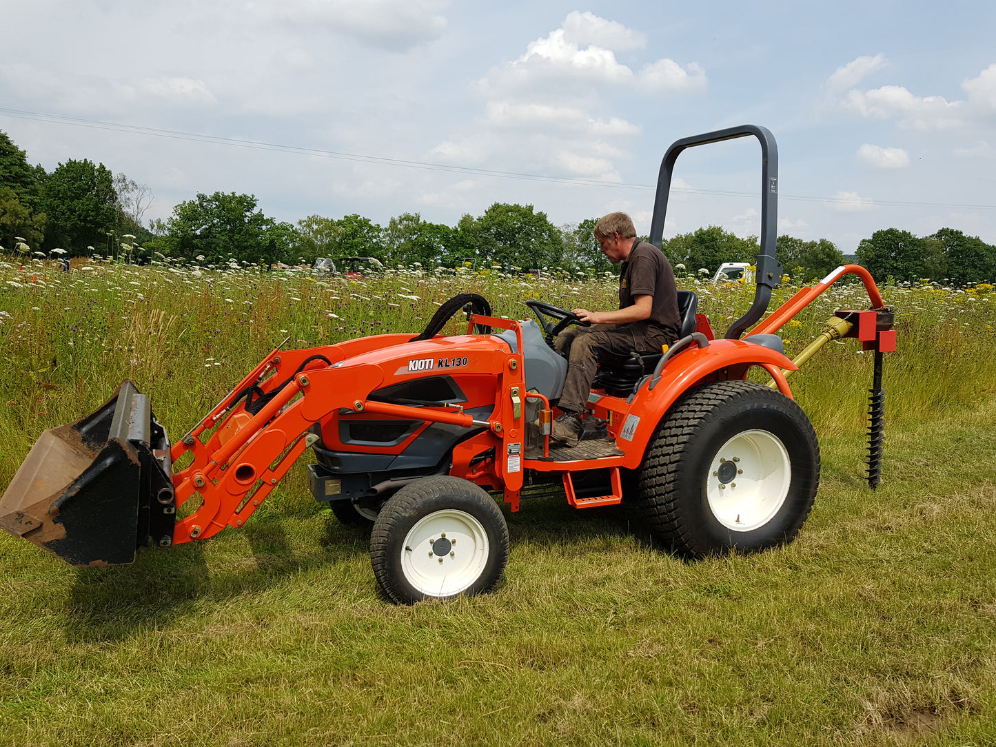 Person operating an orange tractor with FarmMaster tractor post hole borer in a field