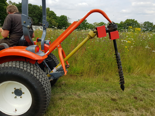 Person operating a tractor with a FarmMaster tractor post hole borer in a field