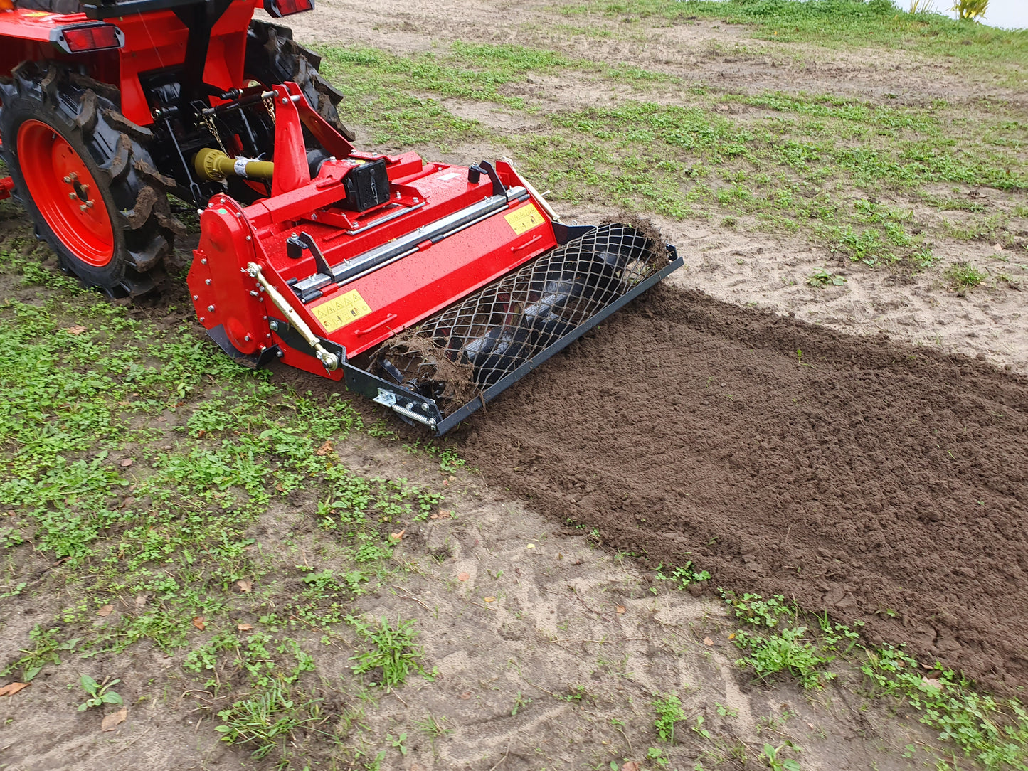 Red tractor with a rotary tiller plowing a field