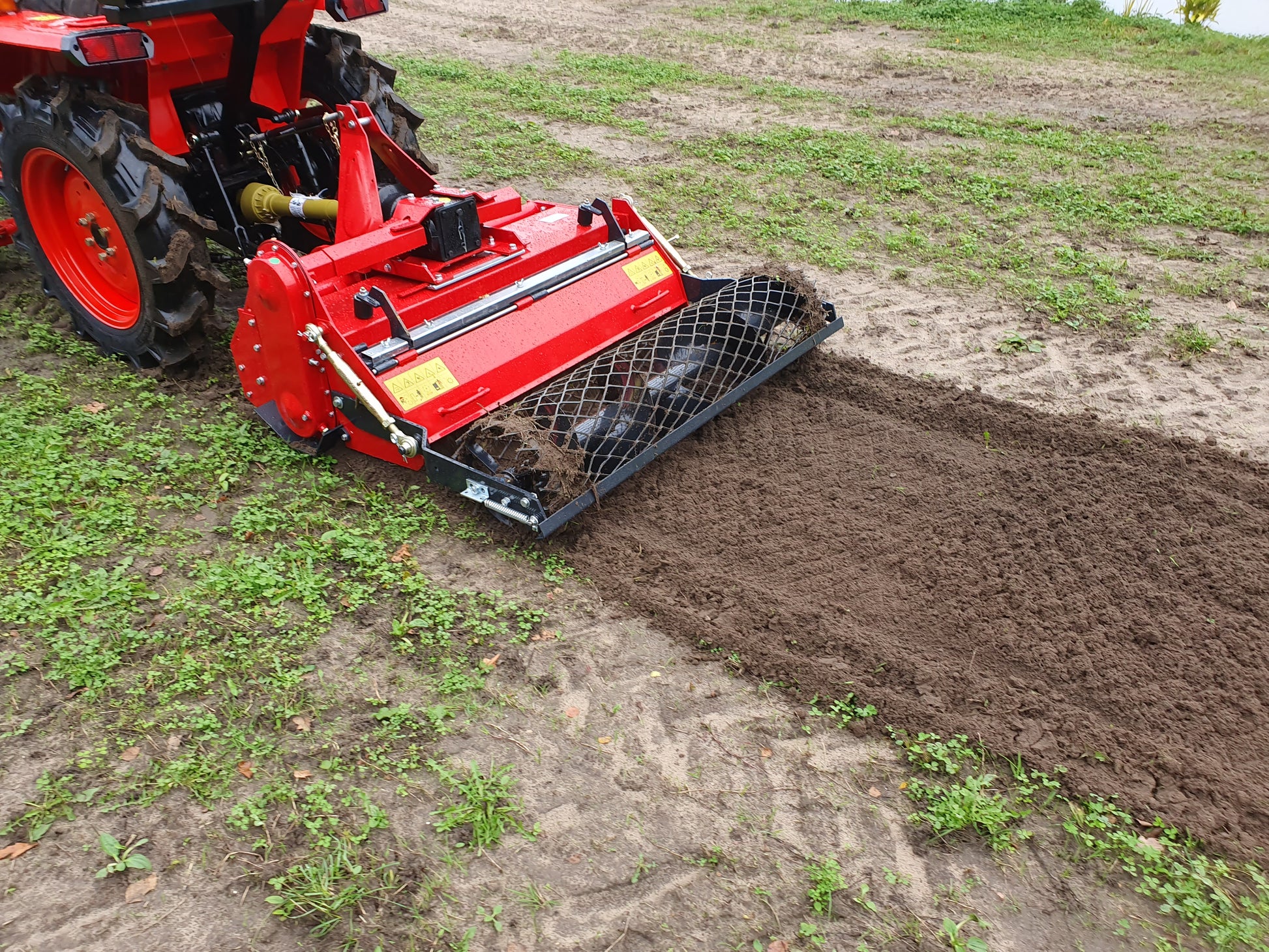 Red tractor with a rotary tiller plowing a field