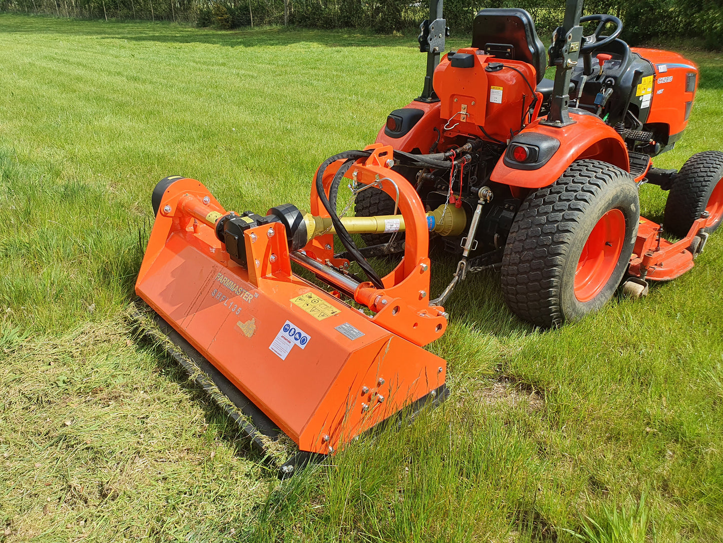 Orange tractor with a large FarmMaster flail mower attachment on a grassy field