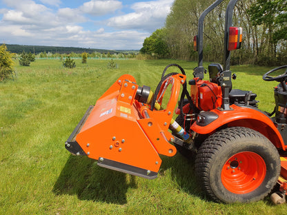 Orange tractor with a FarmMaster offset flail mower attachment on a grassy field under a blue sky with clouds.