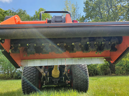Close-up of a FarmMaster offset flail mower attachment on a grassy field with trees in the background