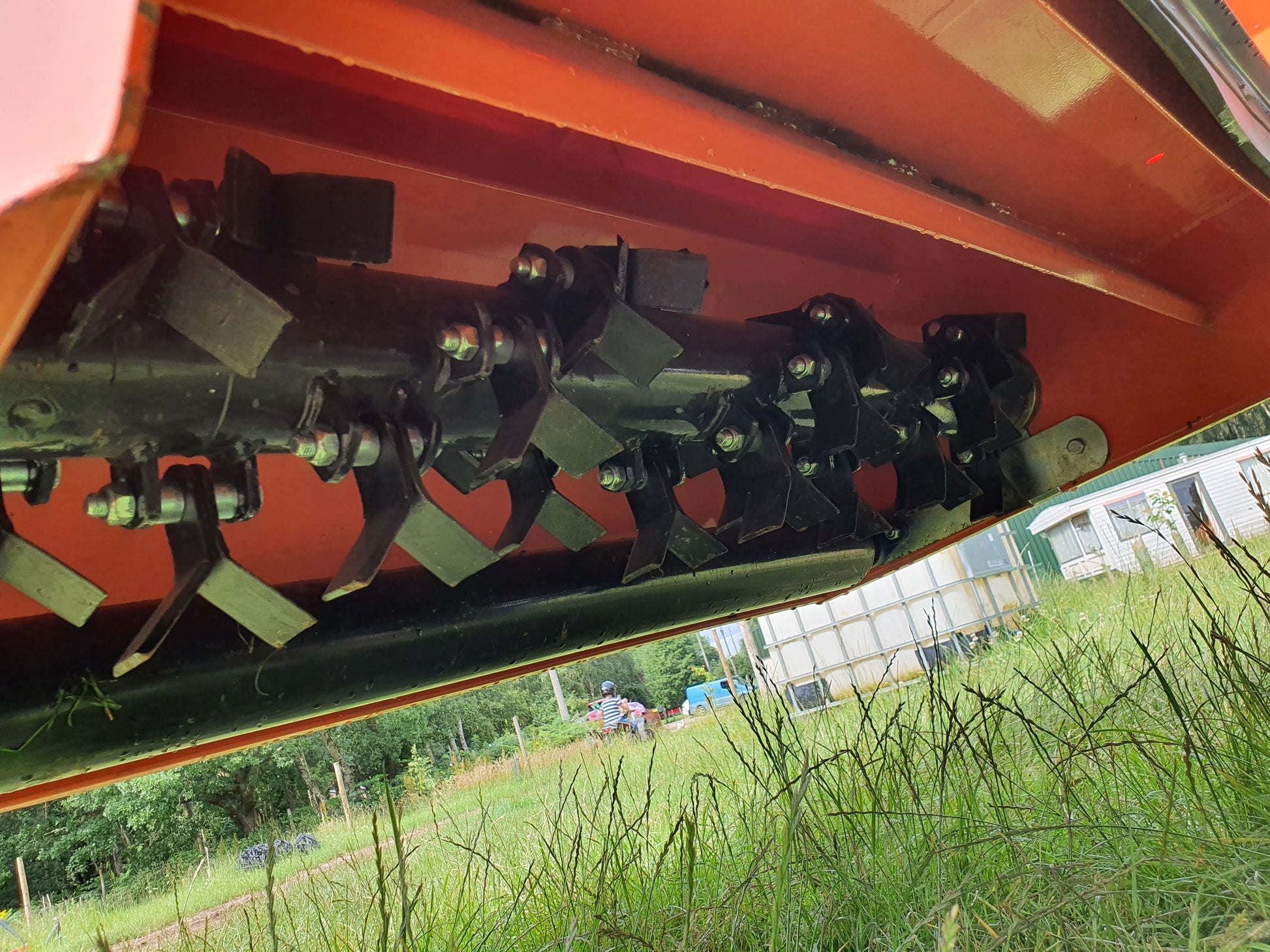 FarmMaster flail collector with a blurred background of greenery and buildings.