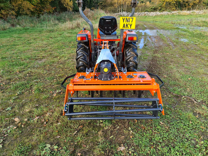 Small orange tractor with a FarmMaster power harrow on a grassy field.