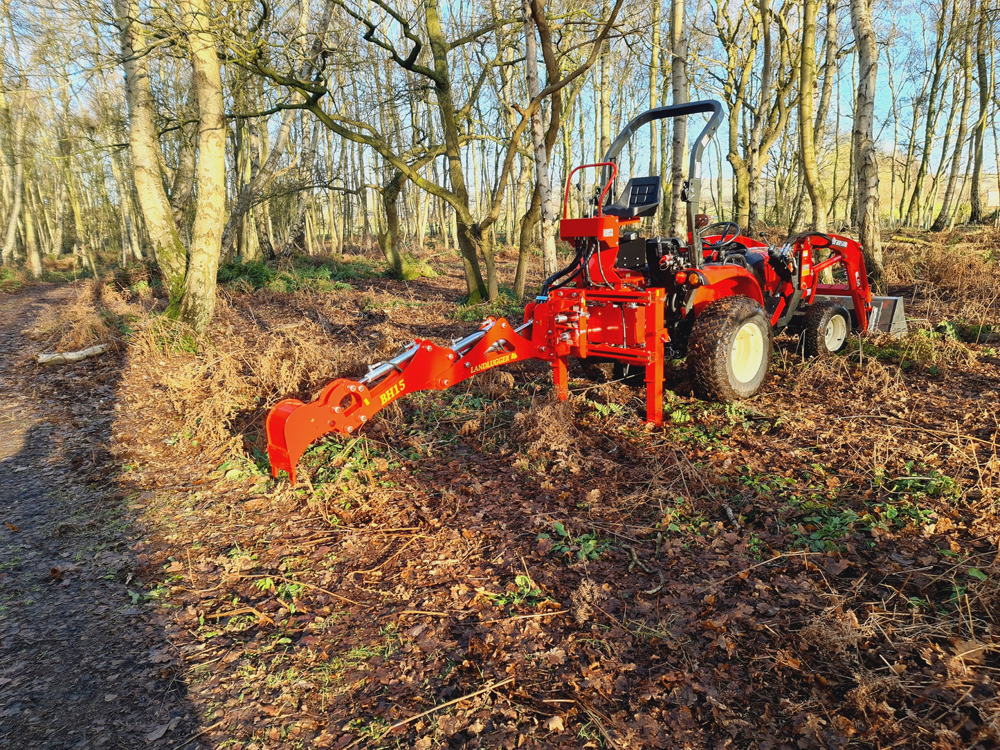 Red tractor with a FarmMaster LandLugger tractor backhoe in a forest setting