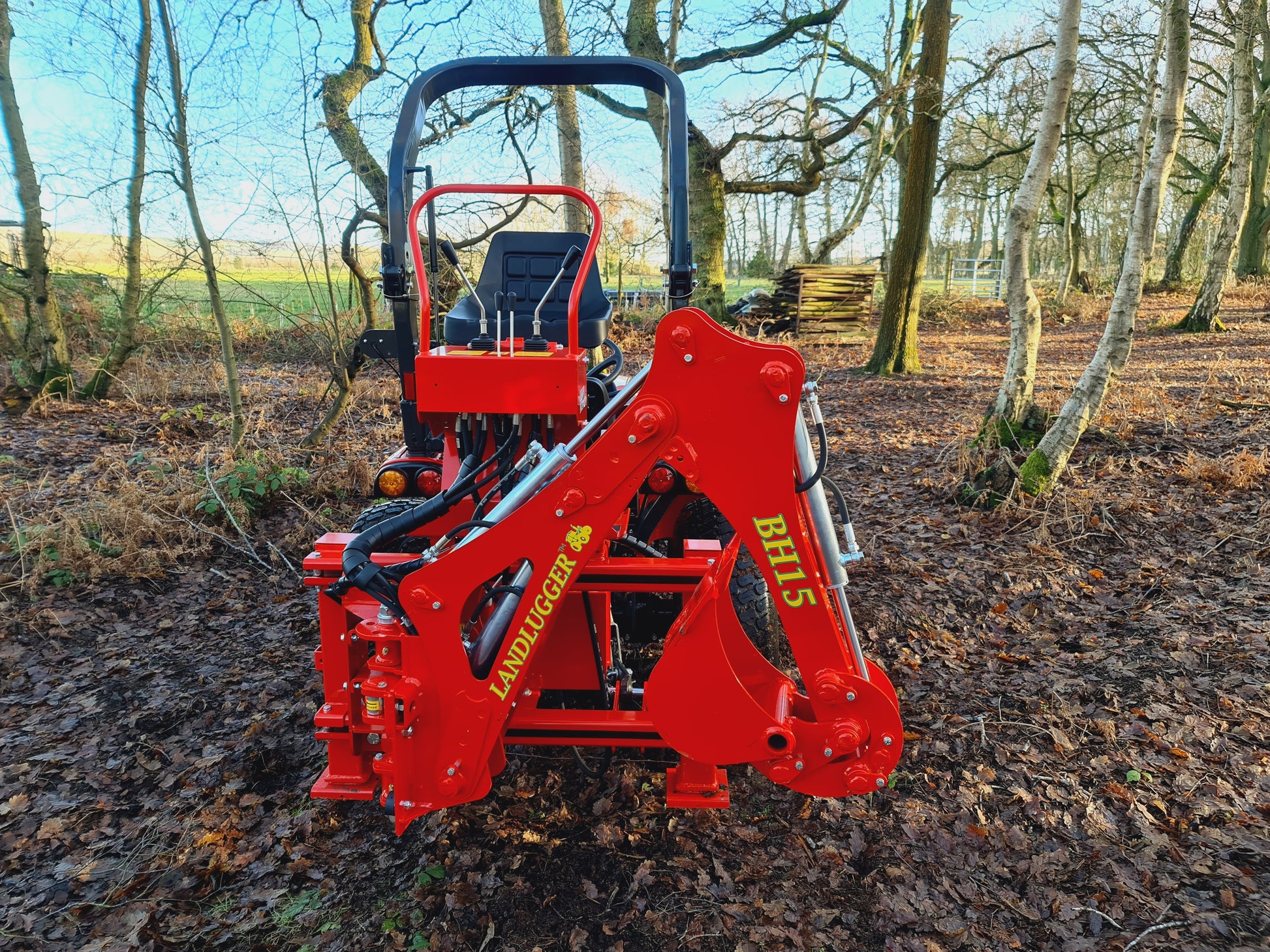 Red compact tractor with FarmMaster LandLugger tractor backhoe in a forested area
