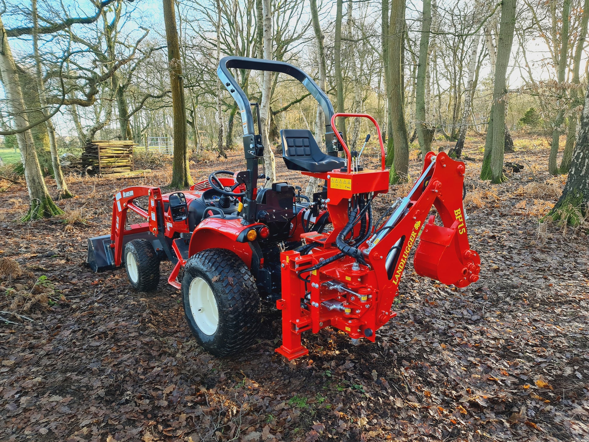 Red tractor with FarmMaster LandLugger tractor backhoe in a forest setting