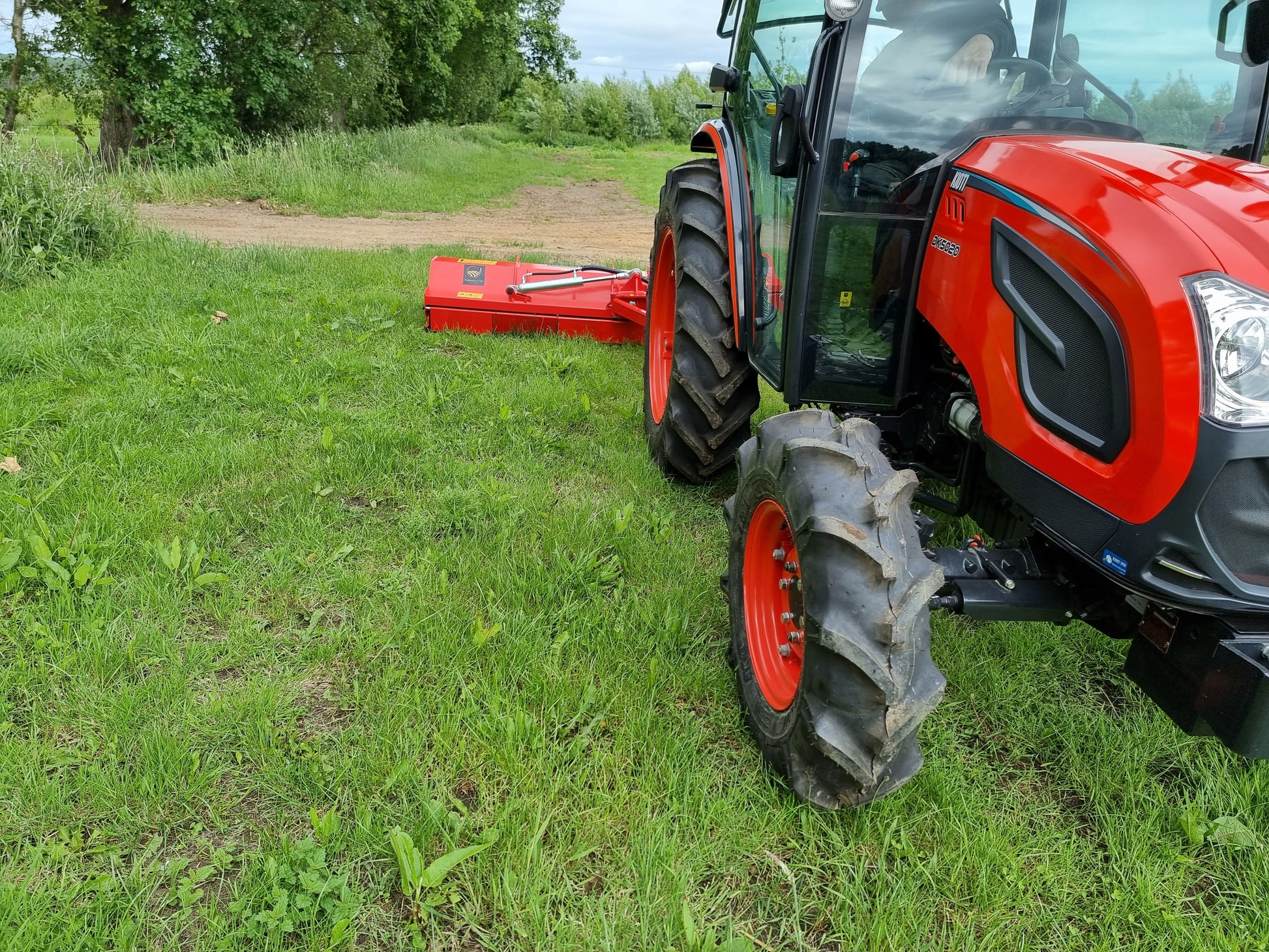 Red tractor on a grassy field with a FarmMaster Pro Verge Flail Mower attached