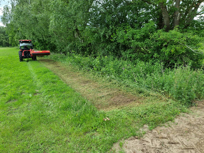 Tractor cutting grass along a path with trees in the background